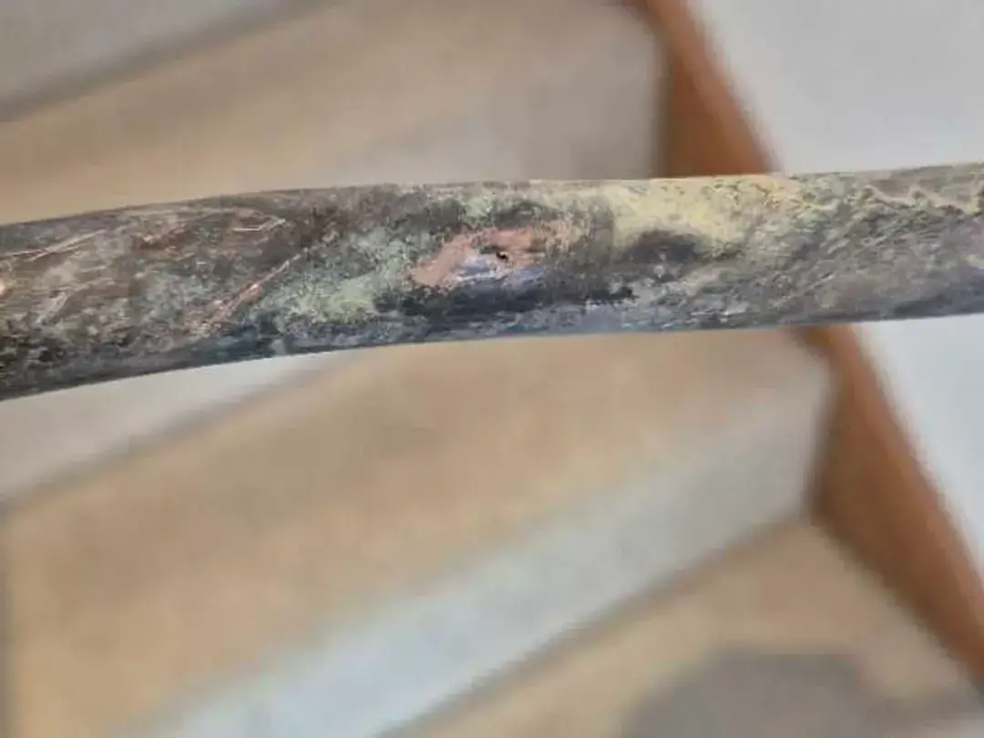 A length of heavily corroded copper pipe held up after being removed from under a floor